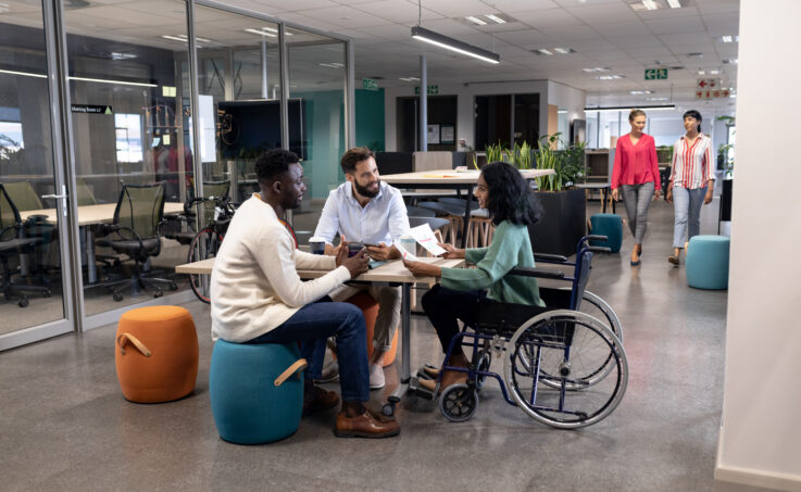 Deux hommes et une femme en fauteuil roulant en réunion dans un bureau. 