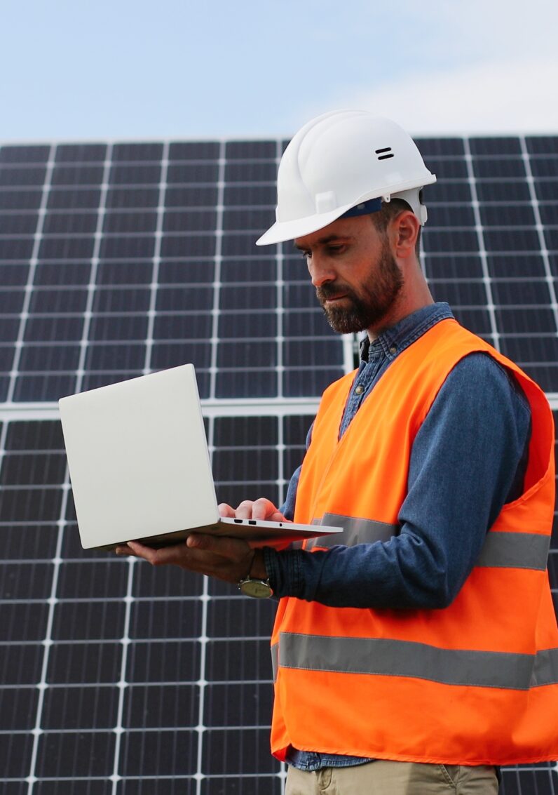 Travailleur du secteur de l’électricité en tenue de sécurité regardant un ordinateur portable devant des panneaux solaires