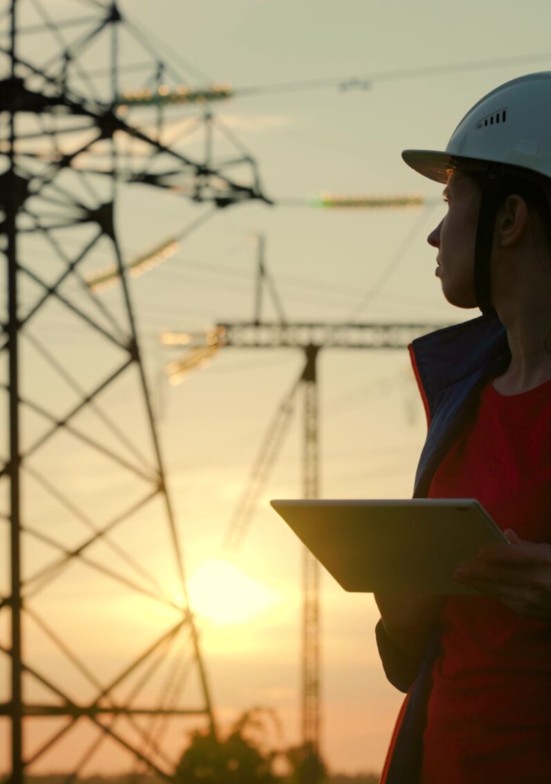 An engineer in a safety helmet checks the power line using a digital tablet. 