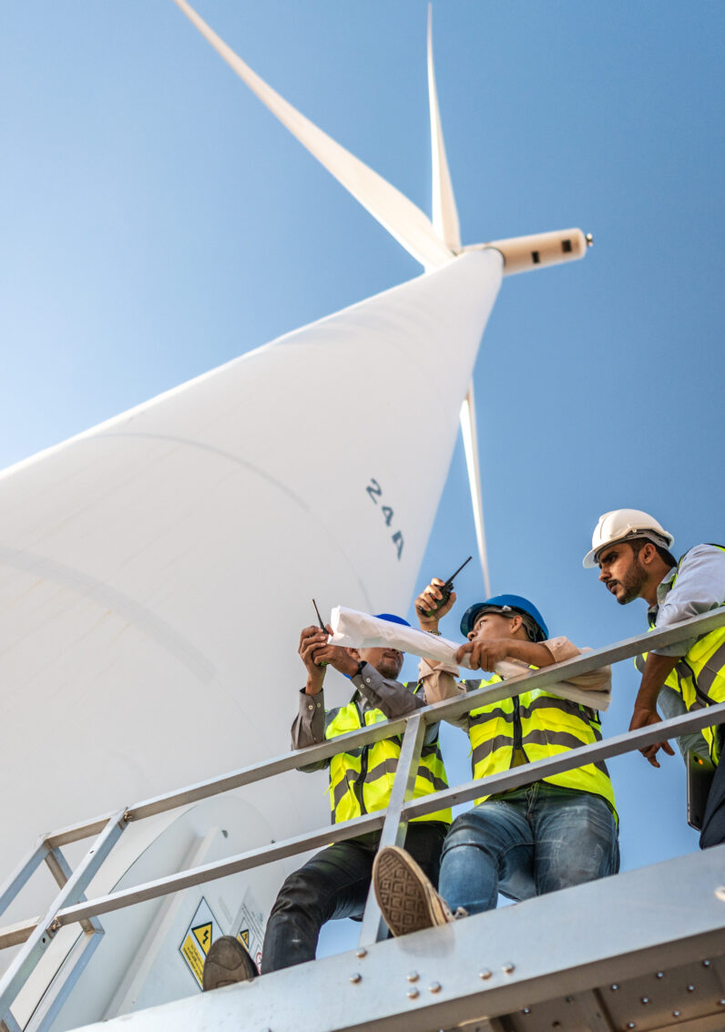 Engineers standing on a platform below a large white wind turbine