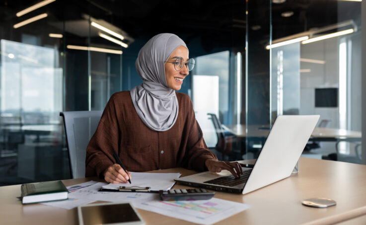 Muslim young woman in hijab working on a laptop