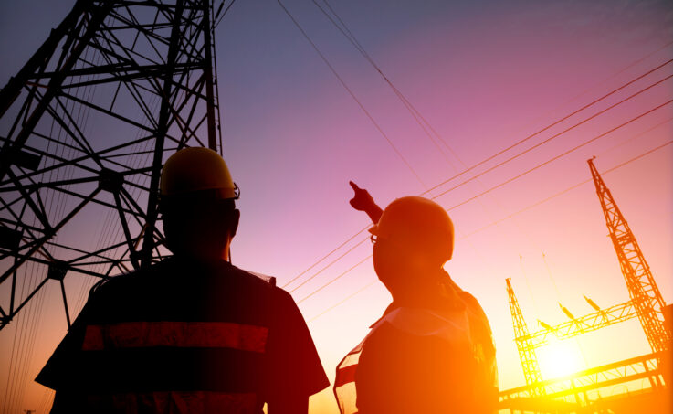 two worker watching the power tower and substation with sunset background