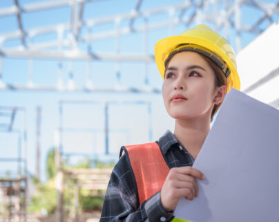 Asian female engineer wear yellow safety hard hat standing and holding blueprint while checking infrastructure