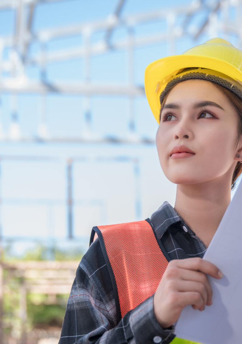 Asian female engineer wear yellow safety hard hat standing and holding blueprint while checking infrastructure