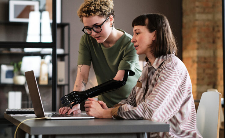 A young professional with a prosthetic arm helping to troubleshoot something with their co-worker