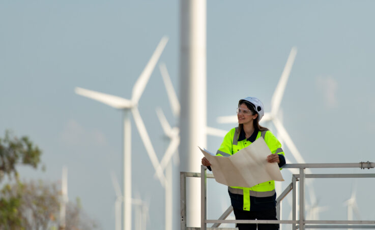 Female wind turbine tech standing in front of a field of turbines