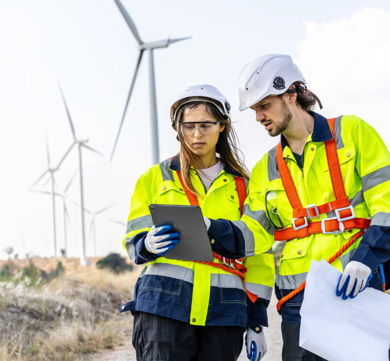 Two engineers working together in the field in front of a row of wind turbines