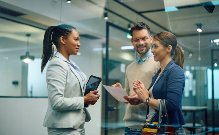 Three office workers reviewing documents together in a glass-walled meeting room.
