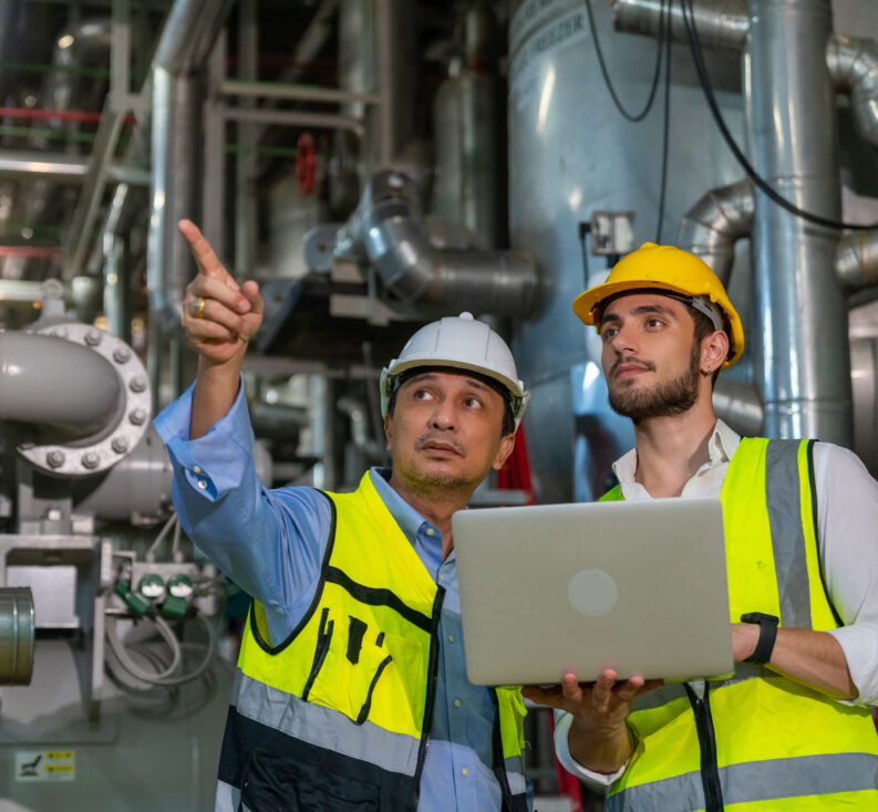 Two professional electrical engineers in safety uniforms working together at factory site control room.