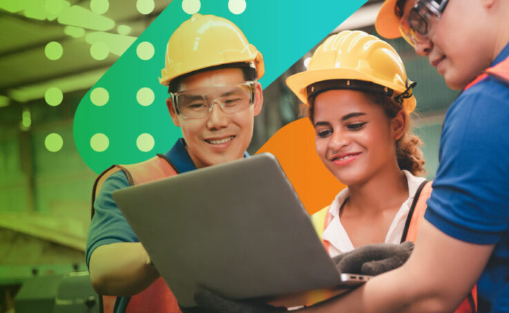 Three employees in hard hats reviewing something together on a laptop
