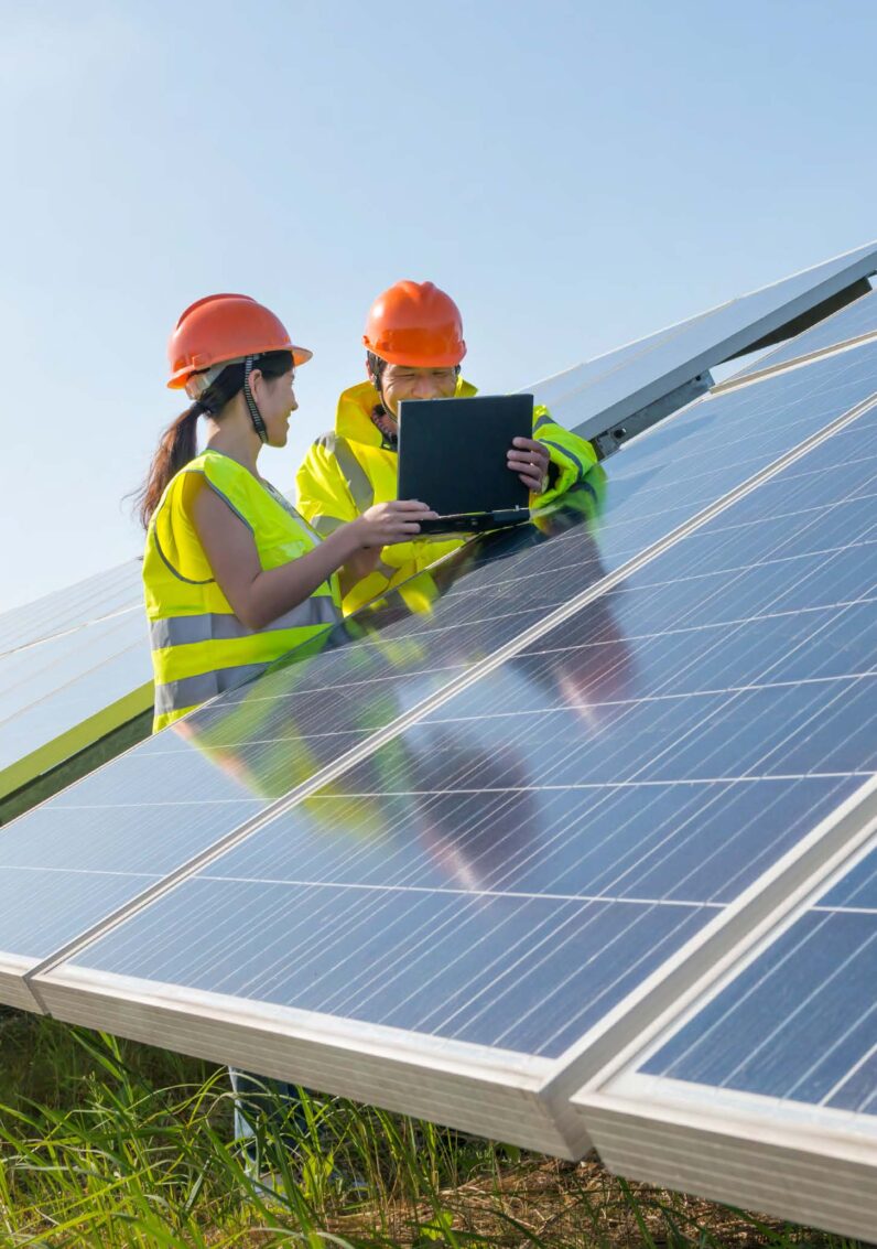 Two electricity industry professionals standing at a solar panel and looking over a laptop