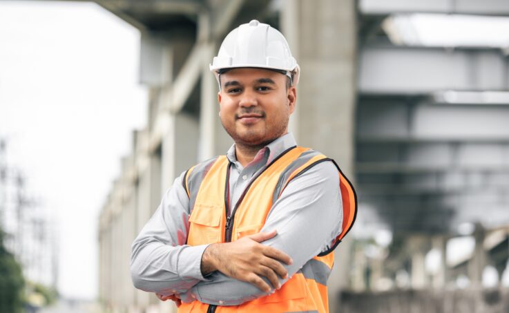 Job site manager wearing a safety vest and a hardhat posing with arms folded. 