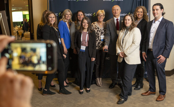 A group of people in business clothing smile for a photo in front of a navy backdrop.