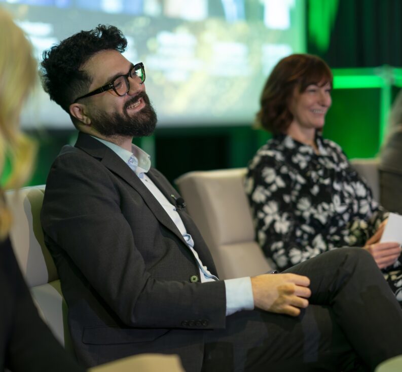 Business people in suits seated at a conference, smiling and engaged in conversation.