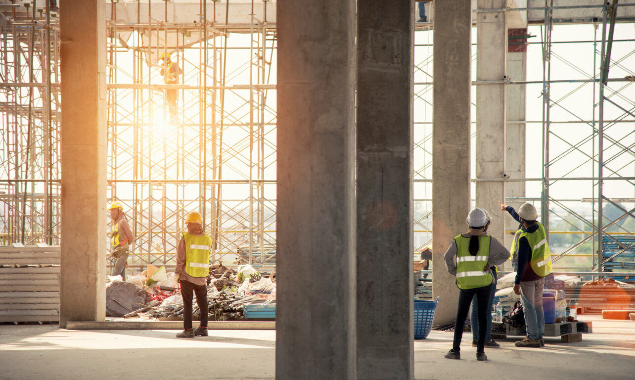 Multiple workers on a job site surrounded by scaffolding, pointing at key parts of the structure