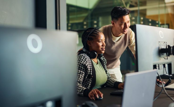 Software engineers collaborating on a project, analyzing code on computer monitors in office