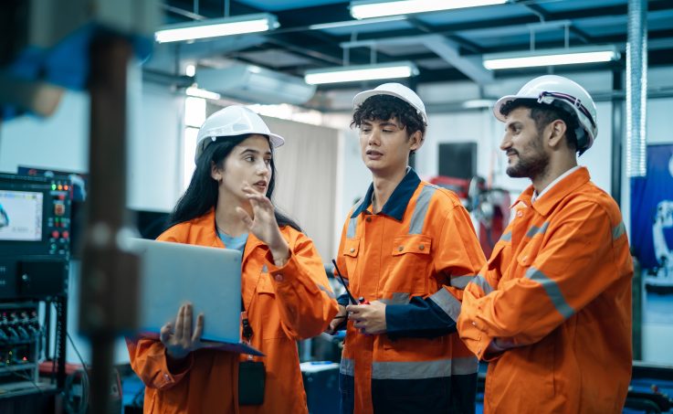 Three engineers in uniform with safety helmet using laptop discussing inspection and maintenance of wind turbine