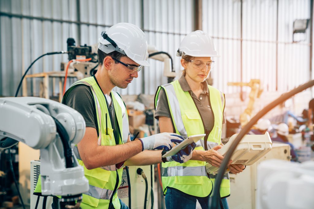 Team of engineers or worker is controlling robot arm machine welding steel, worker using forcing welding with a control screen which is used for precision welding control.