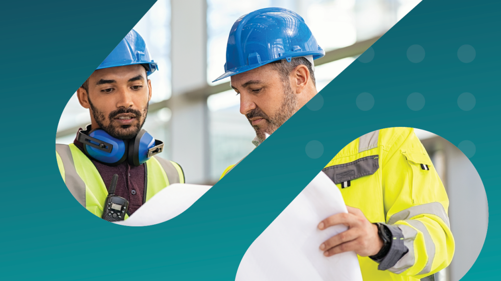 Two construction workers in safety gear reviewing blueprints at a worksite.