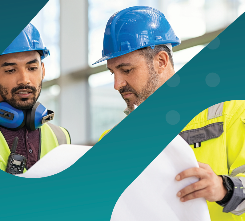 Two construction workers in safety gear reviewing blueprints at a worksite.