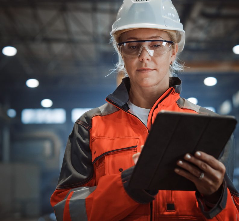 Worker in safety gear using a tablet in an industrial facility.